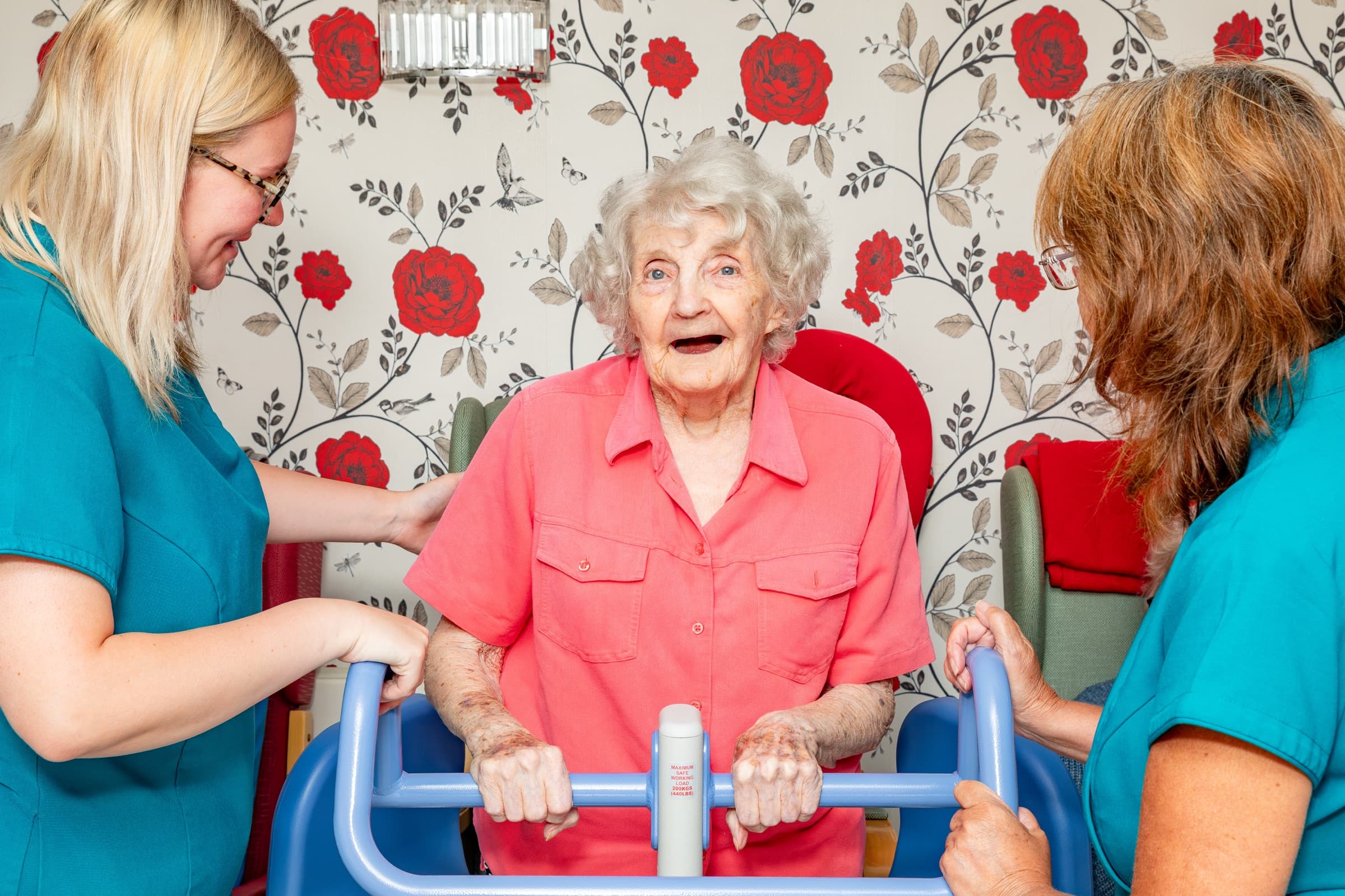 Two staff members supporting a resident with a walking frame